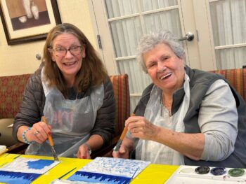 Two women smiling while painting